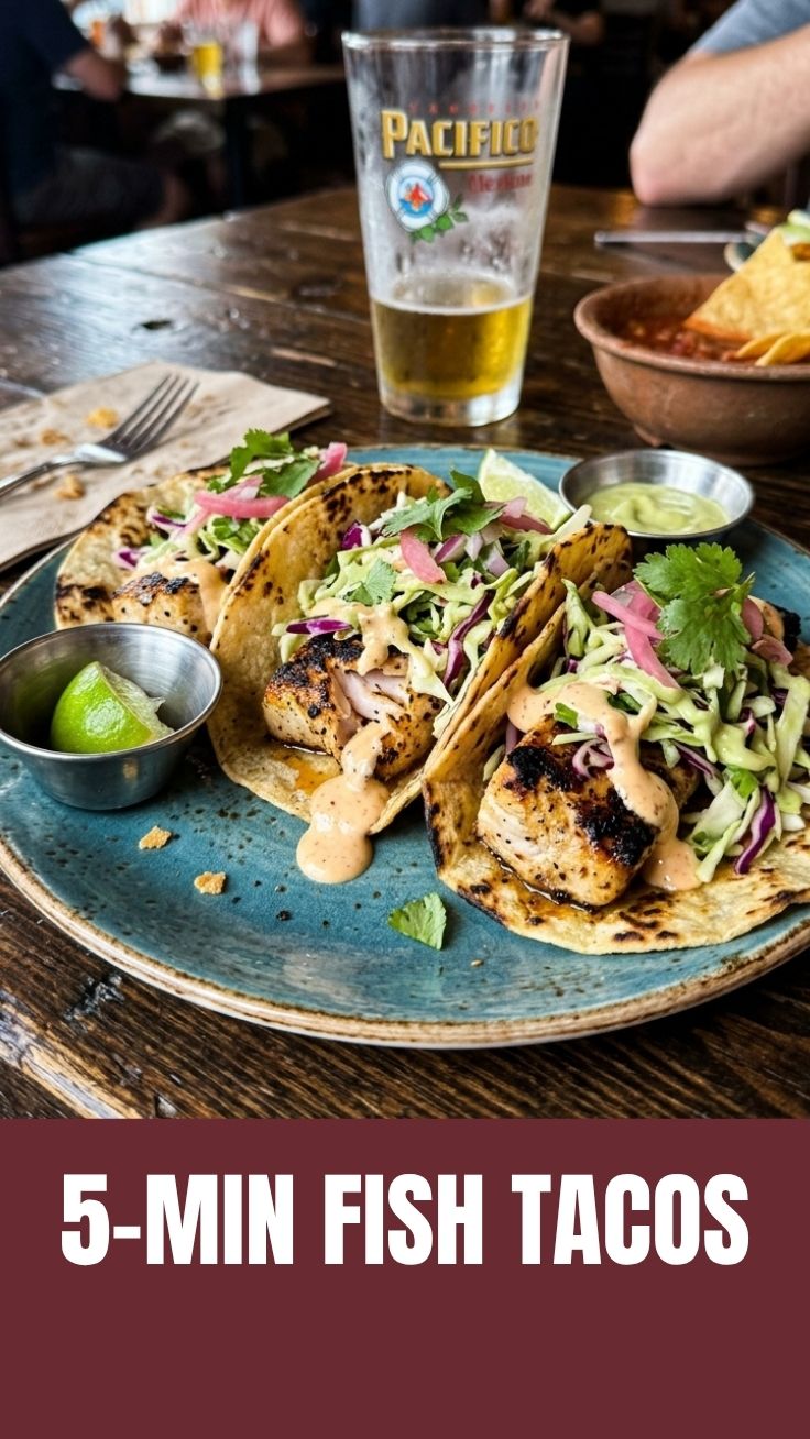 Three grilled fish tacos with vibrant toppings on a dark plate