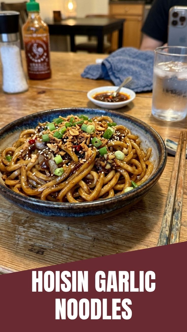 Close-up of hoisin garlic noodles with a glossy sauce and vibrant garnishes