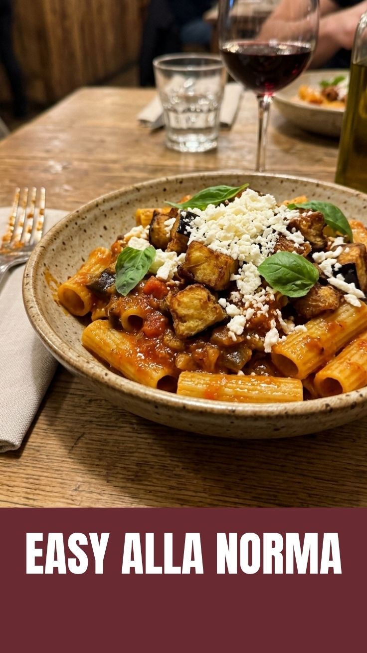A serving of classic Pasta alla Norma featuring penne pasta, fried eggplant, tomato sauce, and grated ricotta salata