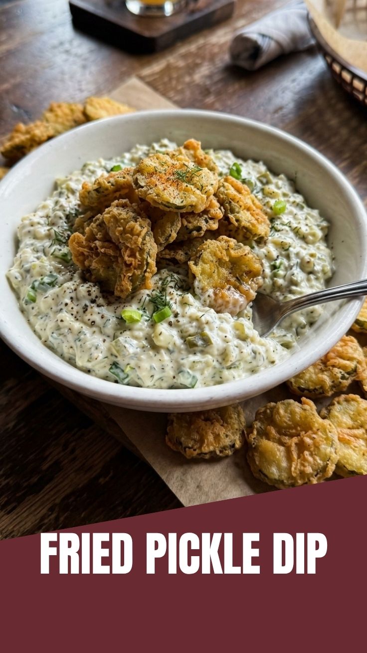 A bowl of creamy fried pickle dip, garnished with fresh dill and fried pickle pieces.